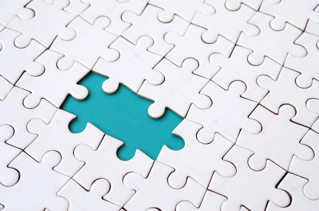 Close-up texture of a white jigsaw puzzle in assembled state with missing elements forming a blue pad for text. Copy space