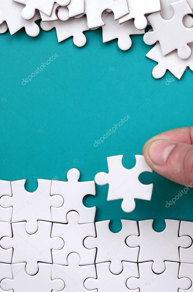 The hand folds a white jigsaw puzzle and a pile of uncombed puzzle pieces lies against the background of the blue surface. Texture photo with space for text