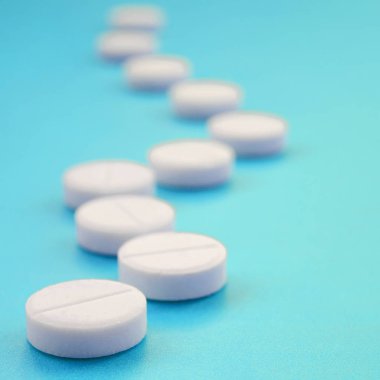 Bir kaç beyaz tabletler bir parlak mavi arka plan yüzeye yalan. İlaç ve tıbbi konularda arka plan görüntüsü