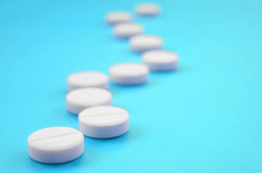 Bir kaç beyaz tabletler bir parlak mavi arka plan yüzeye yalan. İlaç ve tıbbi konularda arka plan görüntüsü