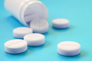 Birkaç beyaz tabletler mavi yüzeyinde plastik kavanozdan düşmek. İlaç ve tıbbi konularda arka plan görüntüsü