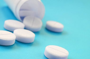 Birkaç beyaz tabletler mavi yüzeyinde plastik kavanozdan düşmek. İlaç ve tıbbi konularda arka plan görüntüsü