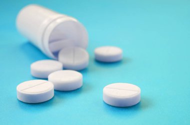 Birkaç beyaz tabletler mavi yüzeyinde plastik kavanozdan düşmek. İlaç ve tıbbi konularda arka plan görüntüsü