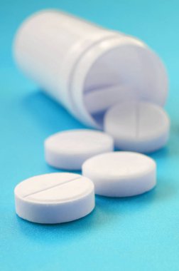 Birkaç beyaz tabletler mavi yüzeyinde plastik kavanozdan düşmek. İlaç ve tıbbi konularda arka plan görüntüsü