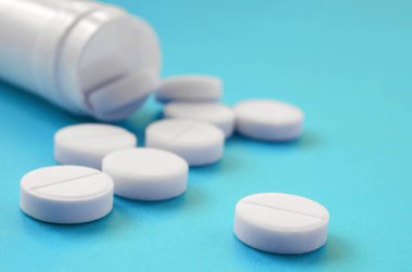 Birkaç beyaz tabletler mavi yüzeyinde plastik kavanozdan düşmek. İlaç ve tıbbi konularda arka plan görüntüsü