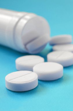 Birkaç beyaz tabletler mavi yüzeyinde plastik kavanozdan düşmek. İlaç ve tıbbi konularda arka plan görüntüsü