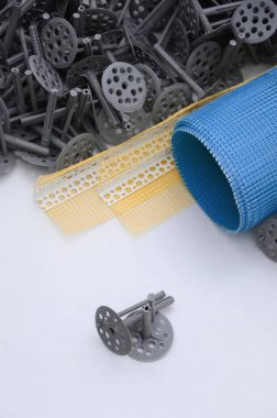 A set of construction items for the insulation of walls. Plastic dowels, a roll of mesh for the insulation of facades and a corner profile with a grid lie on the foam polystyrene surface clipart