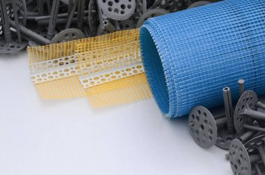 A set of construction items for the insulation of walls. Plastic dowels, a roll of mesh for the insulation of facades and a corner profile with a grid lie on the foam polystyrene surface clipart