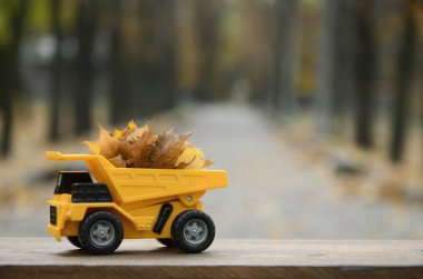 Mevsim sonbahar düşmüş yaprakları hasat kavramı sonbahar park arka planı yapraklarla dolu bir oyuncak sarı kamyon şeklinde tasvir