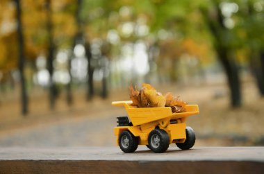 Mevsim sonbahar düşmüş yaprakları hasat kavramı sonbahar park arka planı yapraklarla dolu bir oyuncak sarı kamyon şeklinde tasvir
