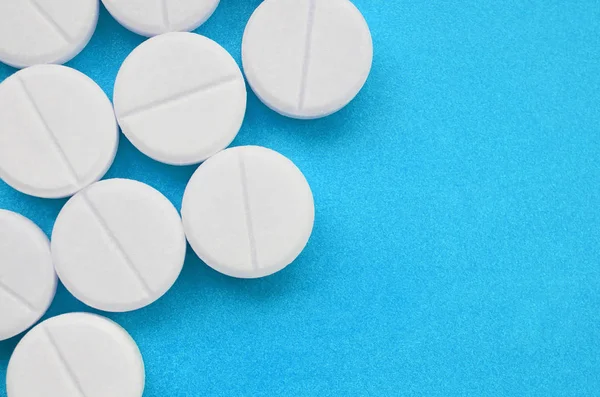 Néhány fehér tabletta feküdjön egy fényes kék háttér felületre. Háttérképet, orvosi és gyógyszerészeti témák — Stock Fotó