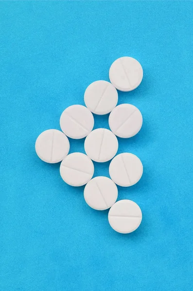 Several white tablets lie on a bright blue background in the form of a triangular arrow. Background image on medicine and pharmaceutical topics — Stock Photo, Image