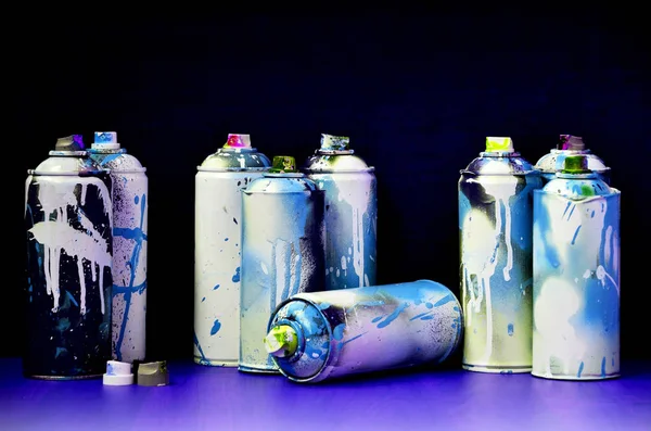 Still life with a large number of used colorful spray cans of aerosol paint lying on the treated wooden surface in the artist's graffiti workshop. Dirty and stained cans for spray art
