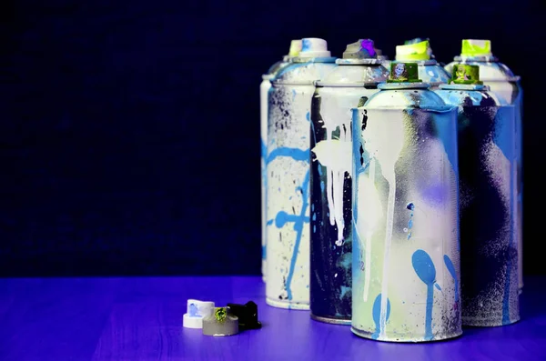 Still life with a large number of used colorful spray cans of aerosol paint lying on the treated wooden surface in the artist's graffiti workshop. Dirty and stained cans for spray art