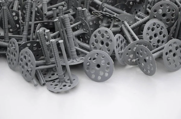 Background of many gray plastic dowels fastening for thermal insulation. A huge pile of plastic bolts with round holey hats lies on a gray foam polystyrene plate — Stock Image Background Many Gray Plastic Dowels Fastening Thermal Insulation Huge Pile Stock Photo