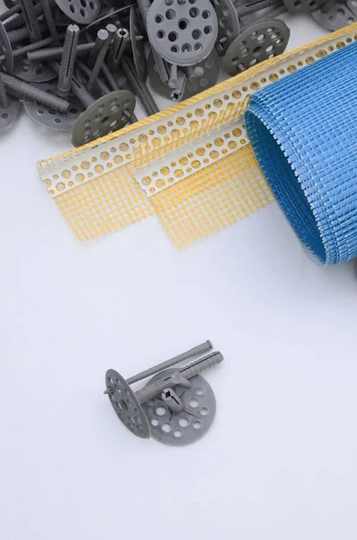 A set of construction items for the insulation of walls. Plastic dowels, a roll of mesh for the insulation of facades and a corner profile with a grid lie on the foam polystyrene surface — Stock Image Set Construction Items Insulation Walls Plastic Dowels Roll Mesh Insulation Royalty Free Stock Images