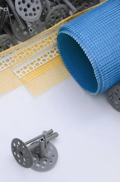 A set of construction items for the insulation of walls. Plastic dowels, a roll of mesh for the insulation of facades and a corner profile with a grid lie on the foam polystyrene surface — Stock Image Set Construction Items Insulation Walls Plastic Dowels Roll Mesh Insulation Royalty Free Stock Images