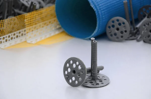 A set of construction items for the insulation of walls. Plastic dowels, a roll of mesh for the insulation of facades and a corner profile with a grid lie on the foam polystyrene surface — Stock Image Set Construction Items Insulation Walls Plastic Dowels Roll Mesh Insulation Royalty Free Stock Photos