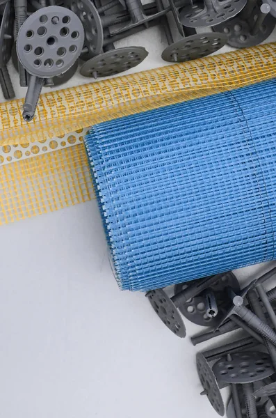 A set of construction items for the insulation of walls. Plastic dowels, a roll of mesh for the insulation of facades and a corner profile with a grid lie on the foam polystyrene surface — Stock Image Set Construction Items Insulation Walls Plastic Dowels Roll Mesh Insulation Royalty Free Stock Photos