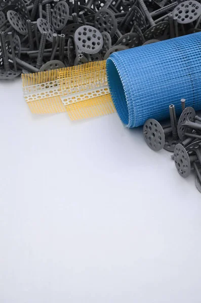A set of construction items for the insulation of walls. Plastic dowels, a roll of mesh for the insulation of facades and a corner profile with a grid lie on the foam polystyrene surface — Stock Image Set Construction Items Insulation Walls Plastic Dowels Roll Mesh Insulation Stock Picture