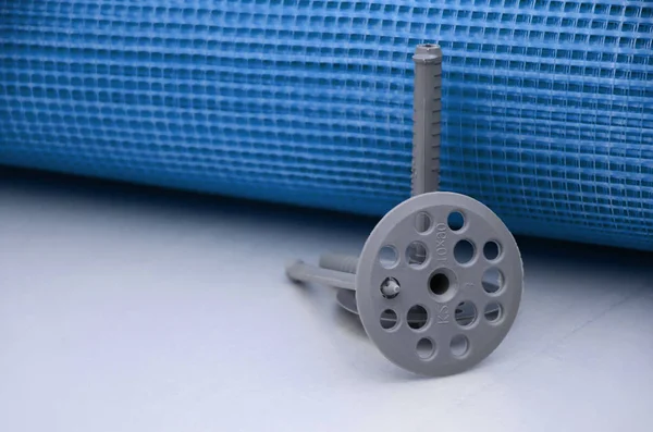 A set of construction items for the insulation of walls. Plastic dowels, a roll of mesh for the insulation of facades and a corner profile with a grid lie on the foam polystyrene surface — Stock Image Set Construction Items Insulation Walls Plastic Dowels Roll Mesh Insulation Stock Picture