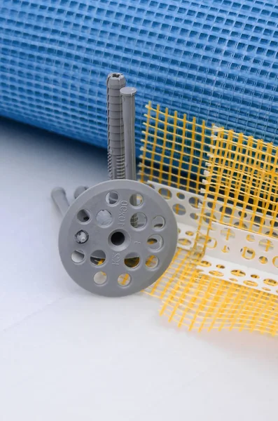 A set of construction items for the insulation of walls. Plastic dowels, a roll of mesh for the insulation of facades and a corner profile with a grid lie on the foam polystyrene surface — Stock Image Set Construction Items Insulation Walls Plastic Dowels Roll Mesh Insulation Stock Picture