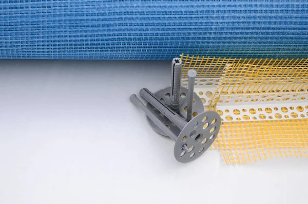 A set of construction items for the insulation of walls. Plastic dowels, a roll of mesh for the insulation of facades and a corner profile with a grid lie on the foam polystyrene surface — Set Construction Items Insulation Walls Plastic Dowels Roll Mesh Insulation Stock Image
