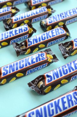 Many Snickers chocolate bars lies on pastel blue paper. Snickers bars are produced by Mars Incorporated. Snickers was created by Franklin Clarence Mars in 1930