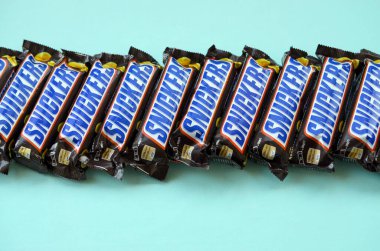 Many Snickers chocolate bars lies on pastel blue paper. Snickers bars are produced by Mars Incorporated. Snickers was created by Franklin Clarence Mars in 1930