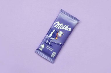 Eflatun arkaplana sarılmış klasik menekşe rengi Milka çikolatası tableti. Milka, 1901 'de İsviçre' de üretilen bir çikolata markasıdır.