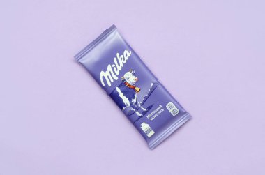Eflatun arkaplana sarılmış klasik menekşe rengi Milka çikolatası tableti. Milka, 1901 'de İsviçre' de üretilen bir çikolata markasıdır.