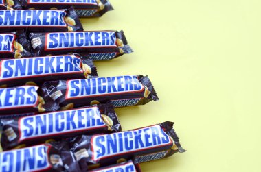 Birçok Snickers çikolatası pastel sarı kağıdın üzerinde yatar. Snickers çikolataları Mars Anonim Şirketi tarafından üretilir. Snickers 1930 yılında Franklin Clarence Mars tarafından yaratıldı.