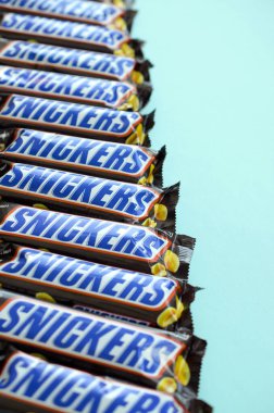 Many Snickers chocolate bars lies on pastel blue paper. Snickers bars are produced by Mars Incorporated. Snickers was created by Franklin Clarence Mars in 1930
