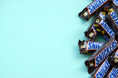 Many Snickers chocolate bars lies on pastel blue paper. Snickers bars are produced by Mars Incorporated. Snickers was created by Franklin Clarence Mars in 1930