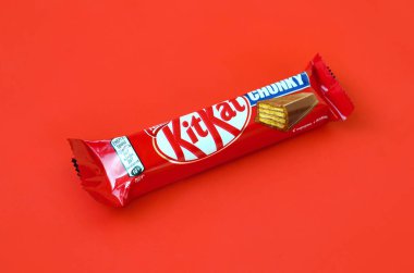 Kit Kat chocolate bar in red wrapping lies on bright red background. Kit kat created by Rowntree's of York in United Kingdom and is now produced globally by Nestle