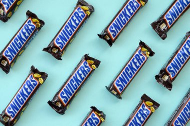 Many Snickers chocolate bars lies on pastel blue paper. Snickers bars are produced by Mars Incorporated. Snickers was created by Franklin Clarence Mars in 1930