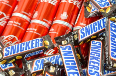 Kahverengi ambalajlı Snickers çikolataları kırmızı Coca Cola kutularının üzerinde duruyor. Meşhur içecek ve çikolata ürünü.