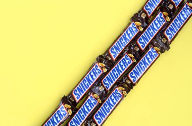 Birçok Snickers çikolatası pastel sarı kağıdın üzerinde yatar. Snickers çikolataları Mars Anonim Şirketi tarafından üretilir. Snickers 1930 yılında Franklin Clarence Mars tarafından yaratıldı.