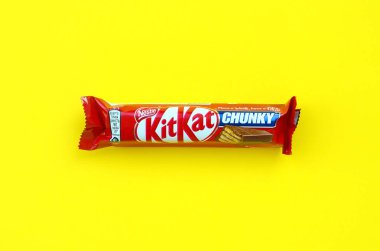 Kit Kat chocolate bar in red wrapping lies on bright yellow background. Kit kat created by Rowntree's of York in United Kingdom and is now produced globally by Nestle
