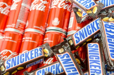 Kahverengi ambalajlı Snickers çikolataları kırmızı Coca Cola kutularının üzerinde duruyor. Meşhur içecek ve çikolata ürünü.