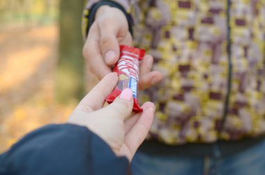 Kharkov, Ukrayna - 21 Ekim 2019: Erkek eli, bir sonbahar parkında kıza bir Kit kat çikolata uzatır. Nezaketin dışavurumu, şekerle tedavi