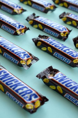 Many Snickers chocolate bars lies on pastel blue paper. Snickers bars are produced by Mars Incorporated. Snickers was created by Franklin Clarence Mars in 1930