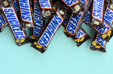 Many Snickers chocolate bars lies on pastel blue paper. Snickers bars are produced by Mars Incorporated. Snickers was created by Franklin Clarence Mars in 1930
