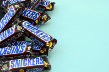 Many Snickers chocolate bars lies on pastel blue paper. Snickers bars are produced by Mars Incorporated. Snickers was created by Franklin Clarence Mars in 1930