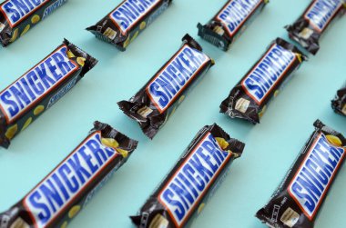 Many Snickers chocolate bars lies on pastel blue paper. Snickers bars are produced by Mars Incorporated. Snickers was created by Franklin Clarence Mars in 1930