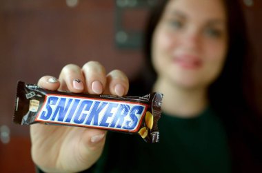 Kharkov, Ukrayna - 8 Ekim 2019: Kafkasyalı genç bir esmer kız Snickers çikolatalarını karanlık odada gösteriyor. Mars yapımı Snickers çikolatası.