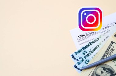 Instagram baskılı logoda 1040 Bireysel Gelir Vergi iade formu ve bej arka planda 100 dolarlık banknotlar bulunur. Sosyal ağ kavramından vergi dönemine yardım