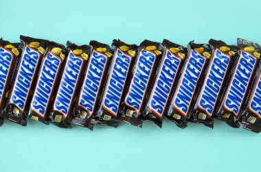 Many Snickers chocolate bars lies on pastel blue paper. Snickers bars are produced by Mars Incorporated. Snickers was created by Franklin Clarence Mars in 1930