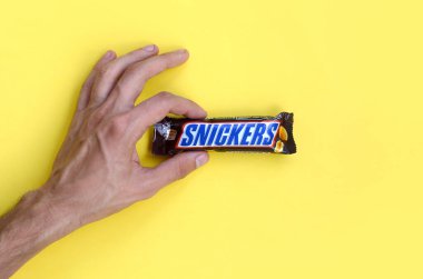 Snickers çikolatası tutarken. Snickers çikolataları Mars Anonim Şirketi tarafından üretilir. Snickers 1930 yılında Franklin Clarence Mars tarafından yaratıldı.