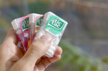 Hand holds three Tic Tac Candy packages of different tastes close up. Tic tac is popular due its minty fresh taste and easy to carry. Hard mints produced by Ferrero since 1968